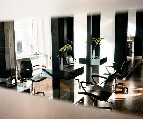 Friseursalon mit schwarzen Stühlen und Spiegeln an einzelnen Arbeitsplätzen, Sonnenlicht fällt durch Fenster