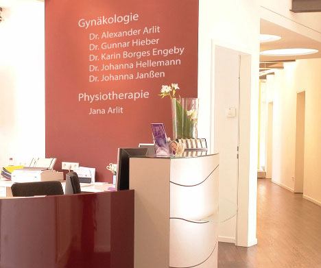 Empfangsbereich einer gynäkologischen Praxis mit roter Wandtafel, auf der die Namen der Ärzte und Physiotherapeutin stehen