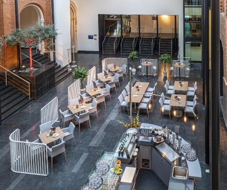 Restaurantbestuhlung mit grauen Sesseln und Holztischen im Lichthof des Alten Rathaus mit schwarzem Marmorboden