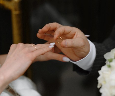 Hände eines Paares bei der Trauung, Bräutigam steckt der Braut einen goldenen Ehering an den Finger
